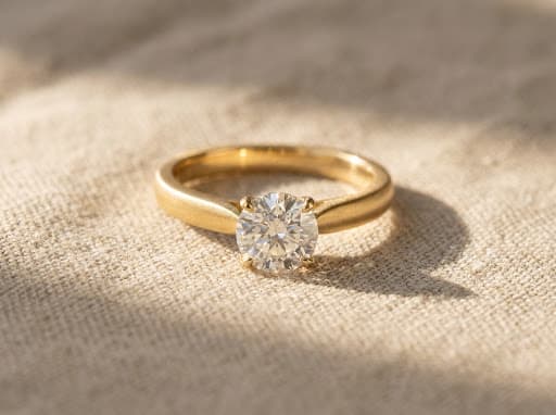 A gold solitaire engagement ring resting on natural linen in warm daylight